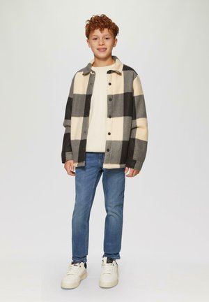 Geruite fleece jas in crème, grijs en zwart, met een knoopsluiting en een platte kraag, gecombineerd met blauwe jeans en witte sneakers.