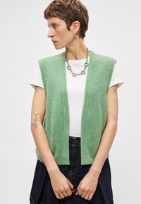 Μέντα πράσινο πλεκτό αμάνικο γιλέκο με υφή, φορεμένο πάνω από λευκό πουκάμισο. Το μοντέλο φοράει ασημένιο κολιέ και σκούρα τζιν φούστα.