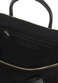 Fekete vászontáska bőr fogantyúkkal, arany cipzárral és bélelt belsővel. Külső cipzáras zsebbel és belső címkével rendelkezik.