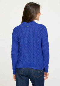 Pull en laine bleu tricoté avec un motif en câble, des poignets et un ourlet côtelés, un design à col montant, et une étiquette à l'arrière.