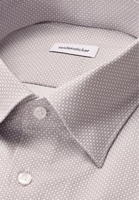 Camicia da uomo grigia chiara con un sottile motivo geometrico, bottoni bianchi e un'etichetta del brand Seidensticker all'interno del colletto.
