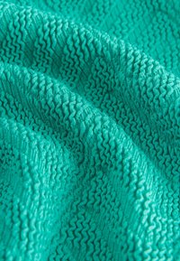 Reljeefne türkiissinine kangas lainelise siksakmustriga. Pind on veidi peegeldav, näidates pehmet ja venivat omadust.