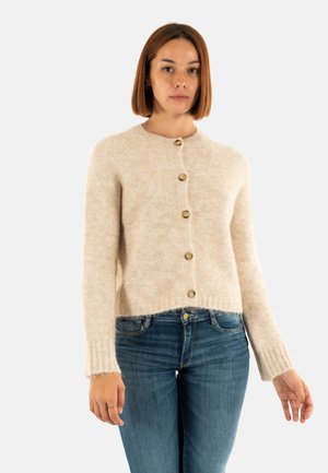 Cardigan en tricot beige avec un col rond, comportant cinq boutons marron, des poignets côtelés et un ourlet court. Porté avec un jean bleu.
