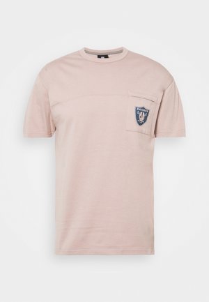 Jasnoróżowa koszulka z krótkim rękawem wykonana z bawełny, z naszywaną kieszonką z czarno-niebieskim logo oraz zaokrąglonym dekoltem.