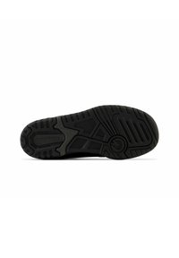 Semelle de chaussure de sport noire avec un motif en caoutchouc texturé, présentant des rainures pour l'adhérence et un détail de logo arrondi près du talon.