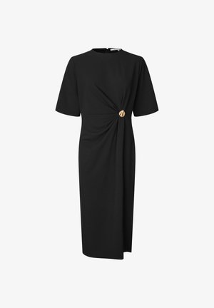 Schwarzes Kleid mit kurzen Ärmeln, das eine gedrehte Gestaltung in der Taille und einen goldenen Knopfakzent aufweist, gefertigt aus einem glatten, strukturierten Stoff.