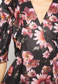 Robe noire avec des motifs floraux roses et pêche, dotée de manches à volants et d'un profond décolleté en V.