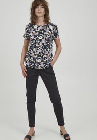 Tumes floraline lühikeste varrukatega topp, millel on lilla, valge ja beež lilledega kaunistus; sobitatud mustade kitsaste pükste ja mustade kontsakingadega.