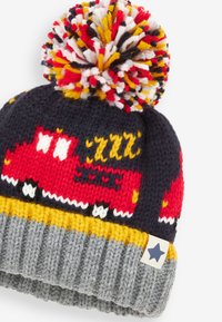 Bonnet tricoté avec une base bleue, motif de camion de pompiers rouge, pompon en fil multicolore et un poignet côtelé gris avec une étoile en accent.