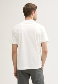 Weißes Kurzarm-Poloshirt mit strukturierter Oberfläche und klassischem Kragen. Das Shirt hat seitliche Schlitze und eine lockere Passform für hohen Komfort.