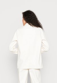 Jaqueta branca de couro sintético com um corte ajustado, mangas longas e uma costura nas costas. Textura suave e design minimalista.