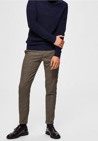 Marinblått stickat tröja, beige och bruna rutmönstrade byxor, samt glänsande svarta mörka skor, med en åtsittande snitt och texturerade detaljer.