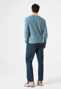 Blauer Strickpullover mit gerippten Bündchen, kombiniert mit dunkelblauer Hose und beigen Sneakern. Der Pullover hat ein strukturiertes Stoffdesign.