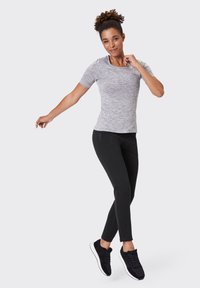 Graues, kurzärmliges, sportliches Oberteil mit strukturiertem Muster; kombiniert mit schwarzen, engen Hosen und schwarzen Turnschuhen mit weißen Sohlen.