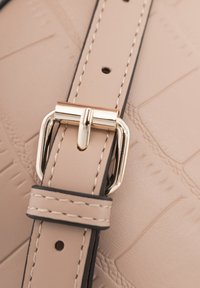 Cinturino in finta pelle beige con una fibbia in metallo dorato, rifinito con cuciture nere. La superficie presenta un leggero motivo testurizzato.