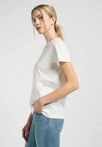 Witte katoenen T-shirt met korte mouwen, ronde hals, voorzien van roze geborduurde accenten bij de kraag. Soepele structuur, casual pasvorm.