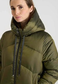 Olijfgroene pufferjack met een hoge, geïsoleerde capuchon, ritsluiting en grijze trekkoorden. Beschikt over een gestikt ontwerp en een glanzende textuur.