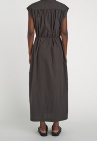 Kvinna i en ärmlös mörkgrå midikjol med insvängd midja, sedd bakifrån, matchad med svarta slip-on sandaler.