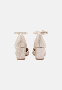 Lesklé zlaté podpätky s blokovým podpätkom, remienkom na členku a otvorenými stranami; s hladkou textúrou a pevnou, zaoblenou zadnou časťou.