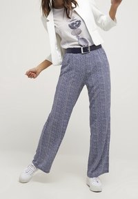 Pantalones de pierna ancha en un patrón de espiga azul y blanco, con una textura de tela suave y una cintura con cinturón, combinados con una blazer blanca.