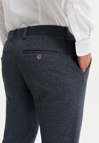 Námořnické vlněné kalhoty tkané do texturovaného herringbone vzoru, se zadními kapsami na knoflíky a přiléhavým pasem.