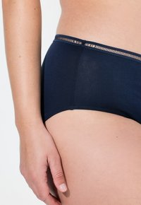 Donkerblauwe dames hipsteronderbroek met een gladde textuur en decoratieve kantafwerking langs de tailleband. Close-up weergave van de stofdetails.