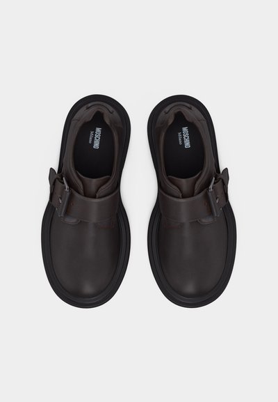 Ζευγάρι σκούρα καφέ δερμάτινα παπούτσια χωρίς κορδόνια με μεγάλες αγκράφες και χοντρές μαύρες σόλες, με την επωνυμία Moschino Milano στο εσωτερικό.