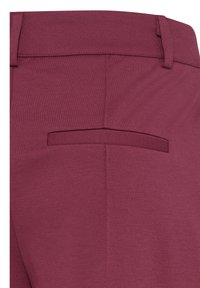 Détail de la poche arrière d'un pantalon bordeaux ajusté avec passants de ceinture, mettant en valeur des coutures nettes et la texture du tissu.