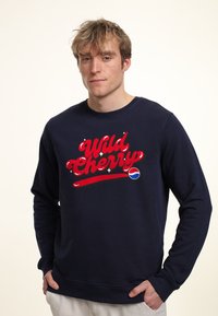Felpa blu navy in misto cotone. Presenta il testo rosso "Wild Cherry" e un piccolo logo Pepsi. Collo tondo classico e polsini a costine.