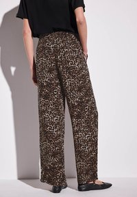 Spodnie szerokie w leopardzi wzór w brązowo-beżowym kolorze, z elastycznym pasem i kieszeniami bocznymi, stylizowane z czarnym topem i płaskimi butami.