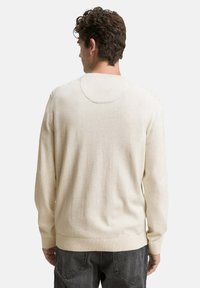 Pull en maille couleur crème avec des manches longues, un col rond et des bords-côtes aux poignets et à l'ourlet. Texture lisse avec des coutures minimales au dos.