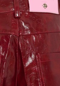 Glanzende donkerrode leren broek met voorzakken en een gestikte zoomdetail, met een gedeeltelijk roze label met een bloemenembleem.