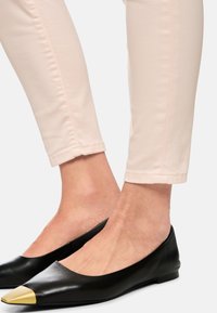Black leather flats with a pointed toe featuring a gold accent. Worn with light pink fitted pants, showcasing smooth texture and sleek design.
