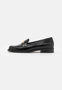 Mocassins en cuir noir avec un bout arrondi, accent doré sur la sangle, petit talon carré, et texture lisse, présentant des détails de couture minimalistes.