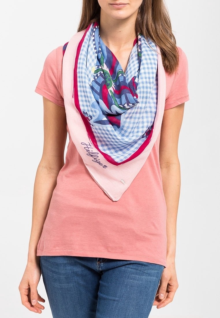 Femme portant un t-shirt rose à manches courtes et un jean bleu avec un grand foulard coloré à motifs autour du cou.