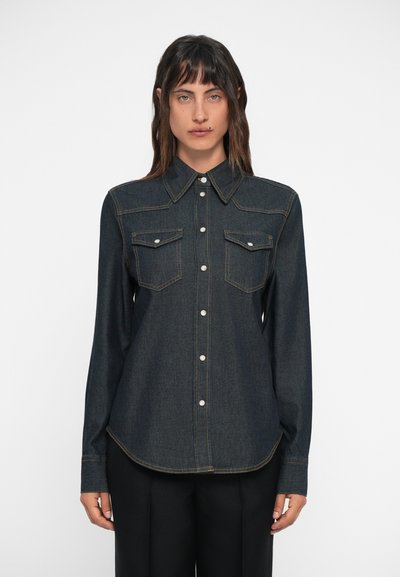 Donkerdenim shirt met een knoopsluiting, puntige kraag, twee borstzakken en contrasterende gele stiksels. Voorzien van lange mouwen en een afgeronde zoom.