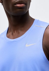 Κοντινό πλάνο ενός ατόμου που φοράει ανοιχτό μπλε αμάνικο αθλητικό τοπ της Nike μπροστά σε ένα μονόχρωμο φόντο.