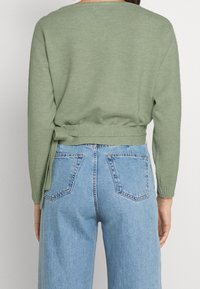 Svetle zelený pletený svetr s volným střihem, se zavazováním v pase. V kombinaci s džíny z lehkého modrého denimu s vysokým pasem.