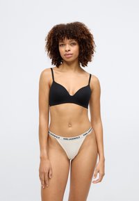 Sorte sømløs BH med justerbare stropper, kombinert med beige tanga med en svart "KARL LAGERFELD" logo livlinje. Glatt tekstur, minimalistisk design.