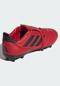 Scarpa da calcio in pelle sintetica rossa con accenti neri, design testurizzato, allacciatura frontale e tacchetti neri sulla suola.