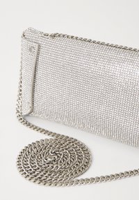 Borsa a busta in rete argentata con superficie testurizzata, con una tracolla a catena arrotolata accanto. Accenti distintivi in metallo.