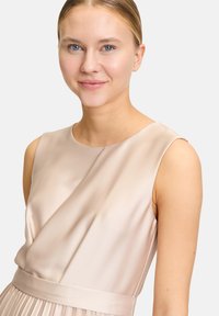 Ein ärmelloses, hellbeiges Kleid aus glattem Stoff, mit rundem Ausschnitt und plissiertem Rock sowie tailliertem Schnitt.