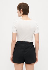 Bijela majica s kratkim rukavima i crne kratke hlače s šarenim pojasom s logom Calvin Klein, prikazane s leđa. Glatka tkanina s prilagođenim dizajnom.