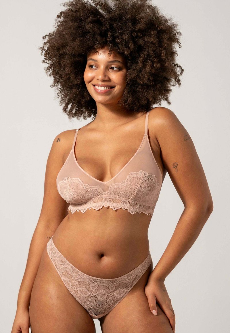  pitsellynder bralette og matchende tang i bløde nude nuancer. Gennemsigtigt stof med blomstermønstre og bølgede kanter. Justerbare stropper inkluderet.