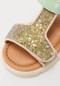 Glittery goldi- ja -vihreät sandaalit, joissa on pehmeä beige sisäpohja, mintunvihreä hihna ja teksturoitu glitteripinta, joka on koristeltu kuusikulmaisilla paljeteilla.