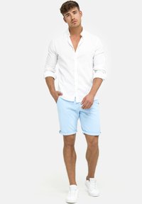 Hvid langærmet skjorte, lyseblå rullede shorts og hvide sneakers. Blødt stof, afslappet design og minimalistiske accenter.