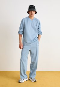 Light blue athletic sweatshirt with a V-neck and matching sweatpants. Features soft fabric and minimal branding. Worn with a black and white bucket hat.