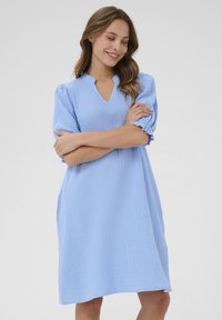 Ljusblå klänning med korta puffärmar och V-hals. Tillverkad av textil med struktur, har en löst sittande passform och sidofickor.