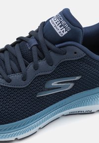 Marinblå Skechers löparskor med nätövre, dämpad mellansula, märkeslogotyp "S" på sidan och "Go Run Consistent 2.0" på tungan.