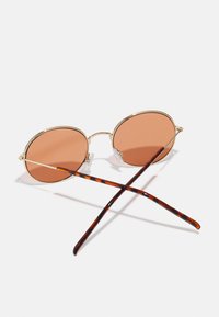 Lunettes de soleil rondes avec verres teintés en rose, monture en métal doré et branches accentuées en écaille de tortue. Design fin et plaquettes de nez ajustables.